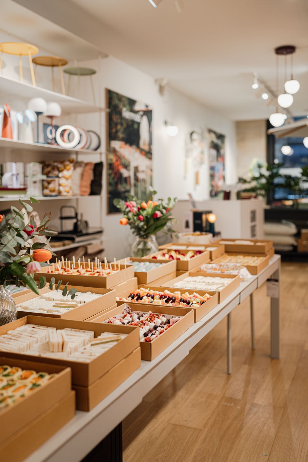 Tables remplis de boîtes de nourriture variée disposées dans une salle bien éclairée avec des bouquets de fleurs.