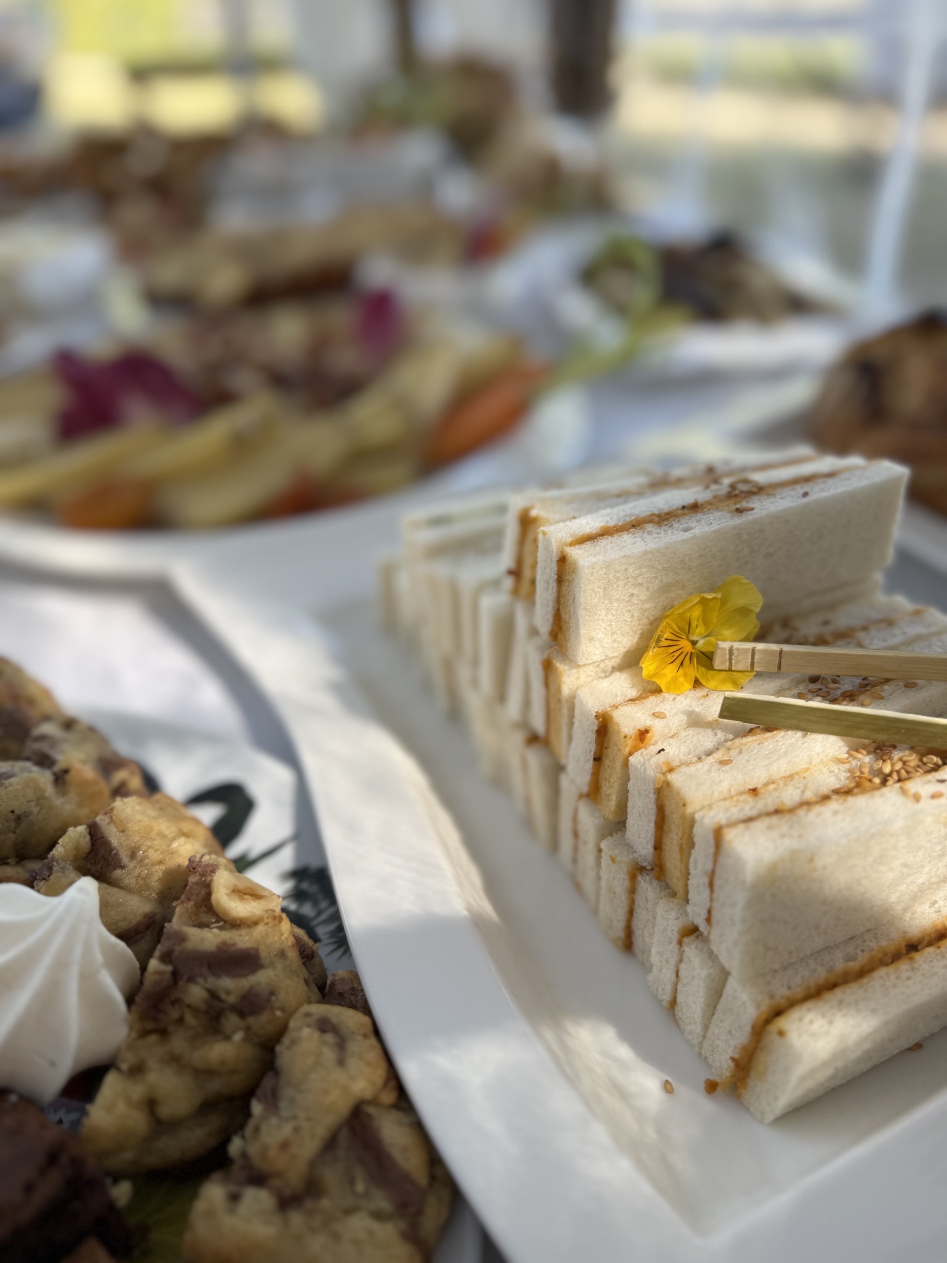 Sandwichs blancs empilés en triangles sur une assiette blanche, décorés d'une fleur jaune tenue par des baguettes en bois.