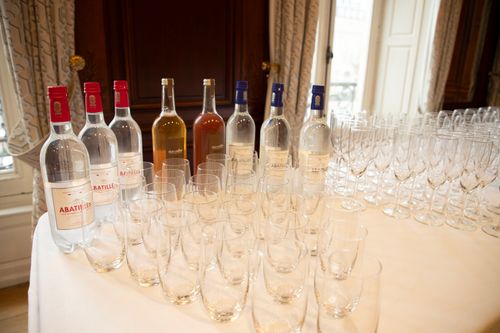 Bouteilles d'eau minérale et de jus avec rangées de verres vides sur une table blanche dans une salle élégante.