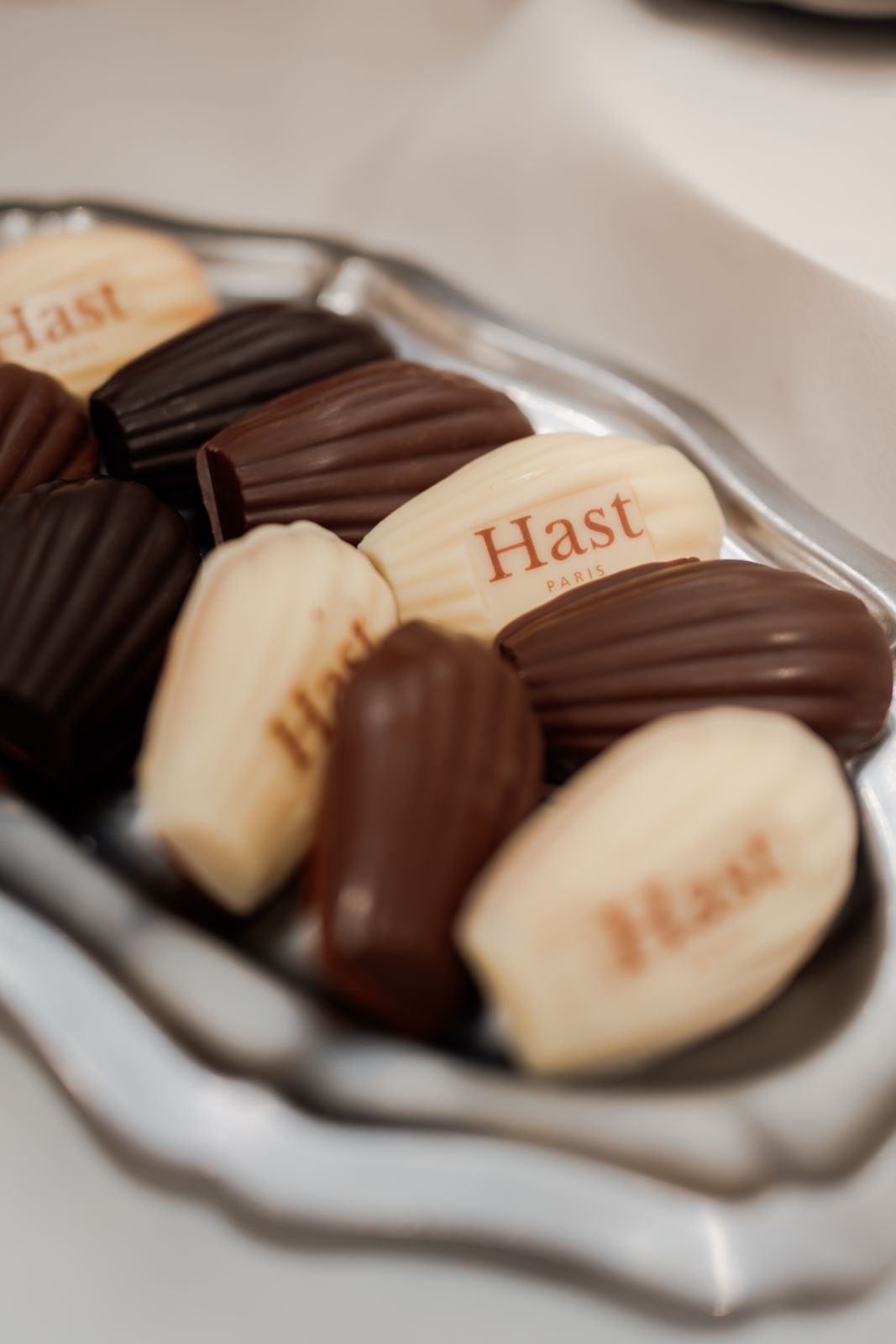 Assortiment de chocolats en forme de madeleines avec inscriptions 'Hast Paris' sur un plateau argenté.