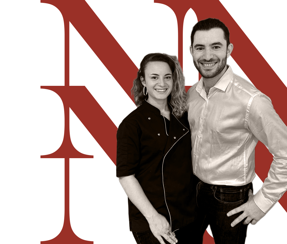 Portrait de deux personnes souriantes, une femme en veste noire et un homme en chemise blanche, sur un fond avec de grandes lettres rouges.