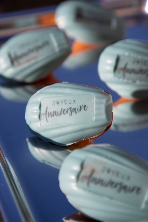 Madeleines bleues glacées avec une étiquette disant « Joyeux anniversaire » sur une surface réfléchissante.