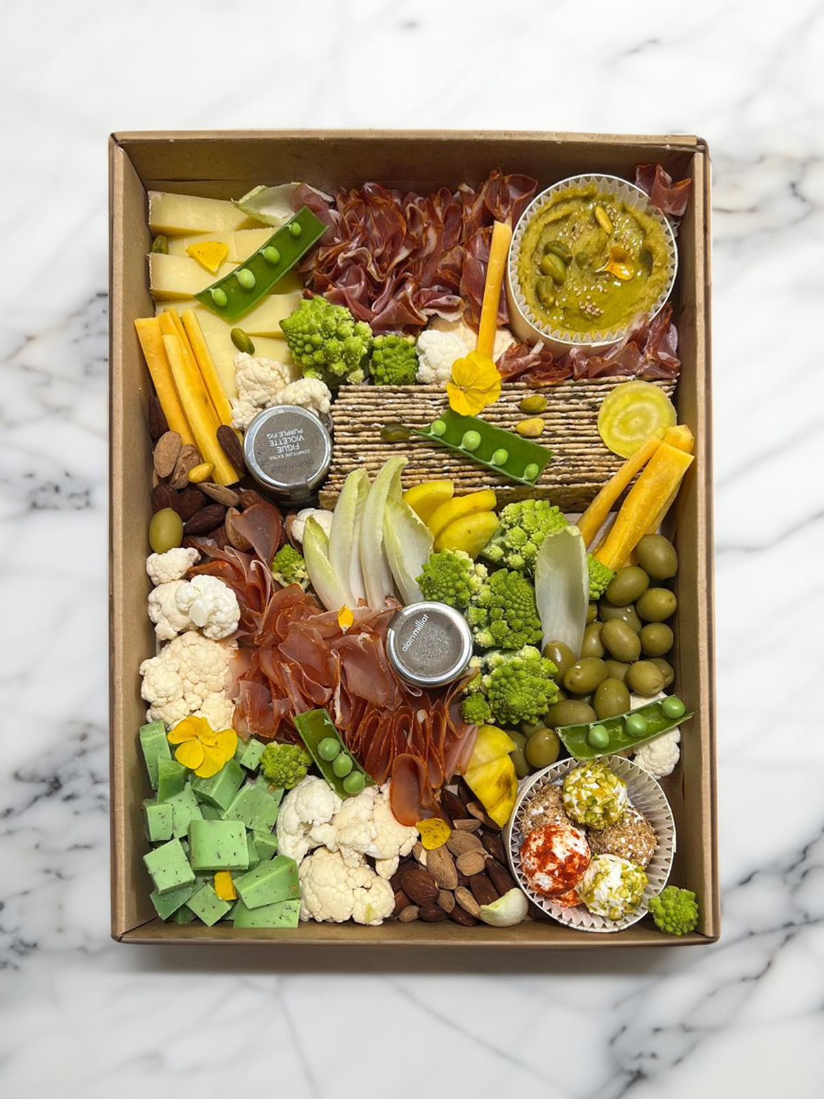 Boîte de charcuteries et légumes assortis avec fromage, olives, crackers, noix et dips sur fond en marbre.