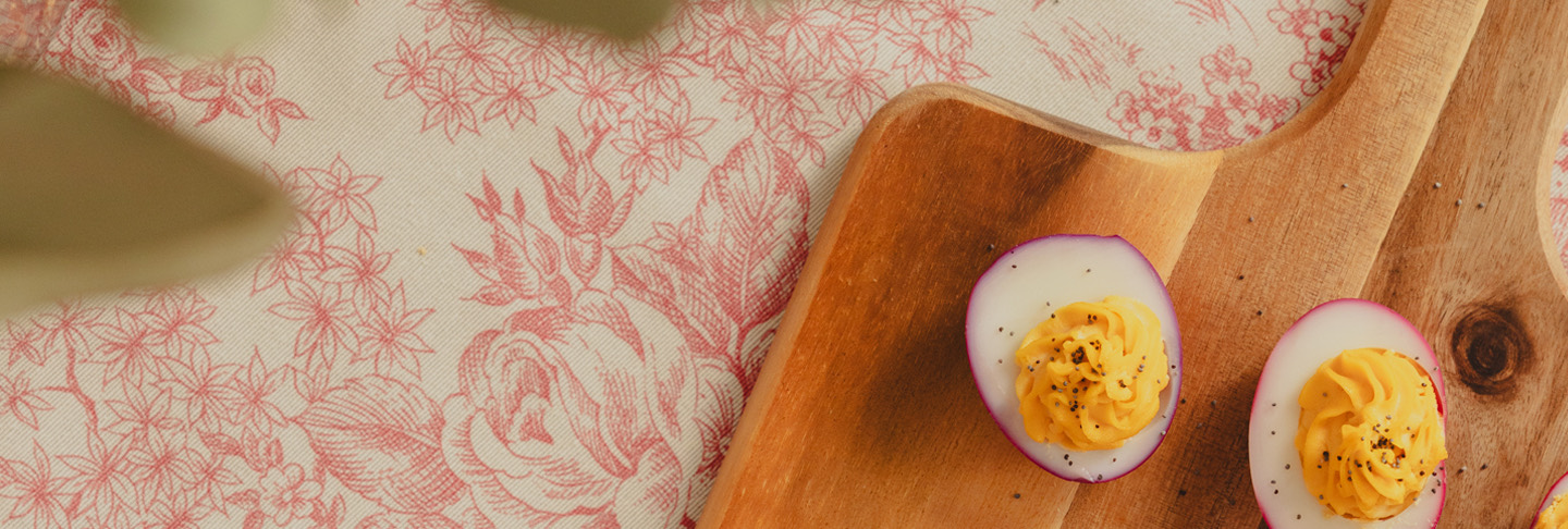 Deux œufs farcis sur un planche en bois posée sur une nappe fleurie rose et crème.