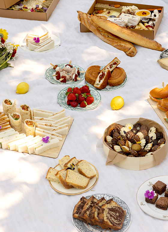 Table nappée blanche avec assortiment de sandwichs, pains, pâtisseries, fruits rouges, biscuits, et chocolats pour un déjeuner champêtre.