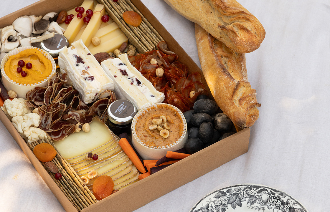 Plateau de charcuterie et fromage avec deux baguettes, crackers, légumes, noix, fruits secs, et petits pots de sauces.