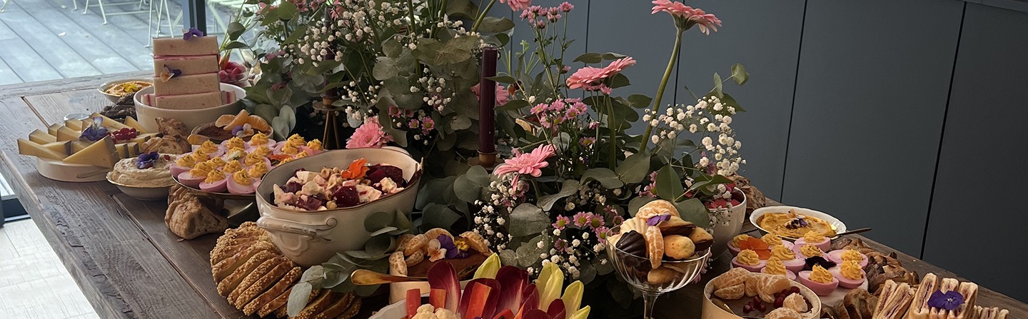 Table dressée en extérieur, ornée de fleurs roses et blanches, garnie de plats salés et de desserts présentés avec soin.