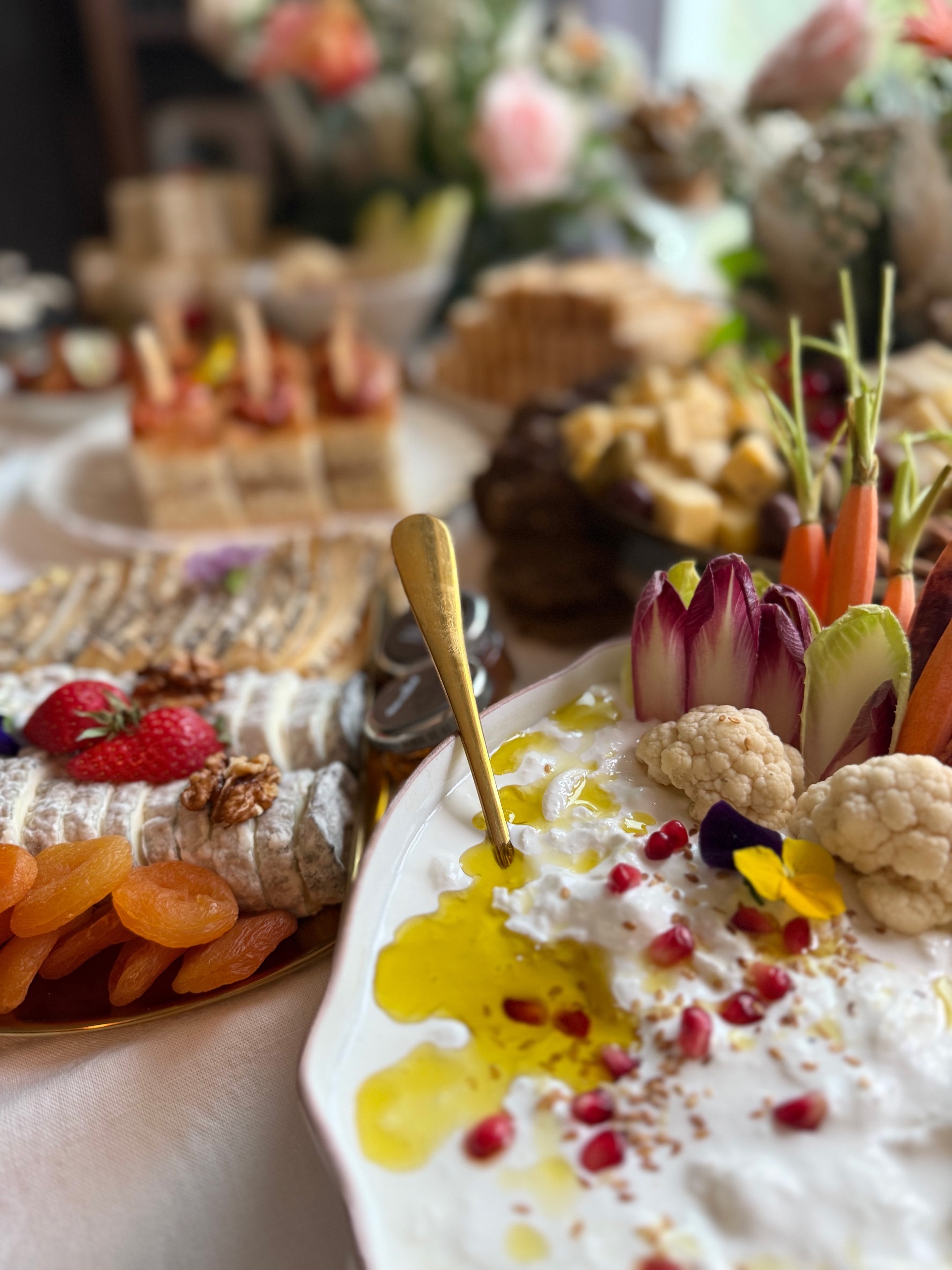 Plateau de fromages, abricots secs, fraises et noix à côté d'un bol de trempette garnie d'huile d'olive, graines, grains de grenade, chou-fleur, carottes et feuilles de radicchio.