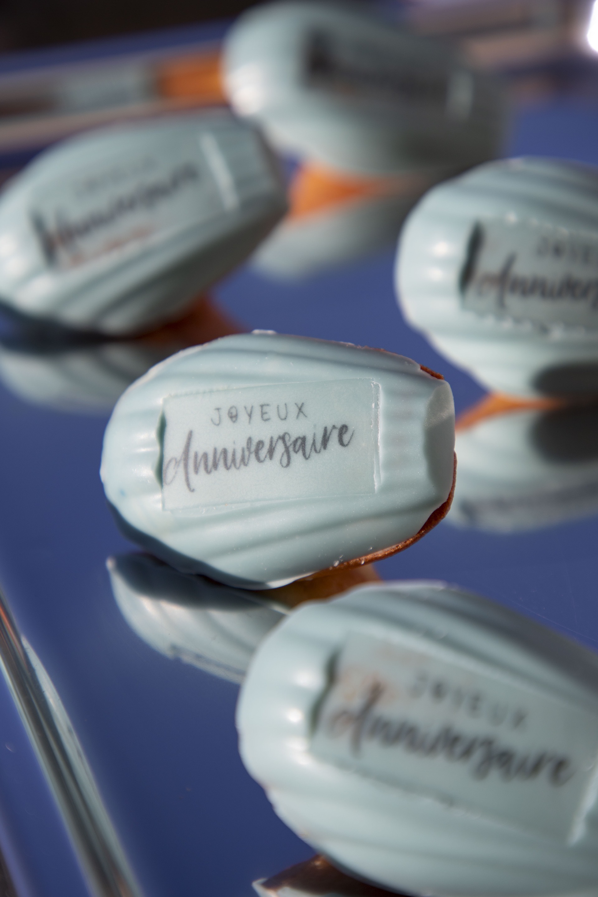Madeleines bleues glacées avec une étiquette disant « Joyeux anniversaire » sur une surface réfléchissante.